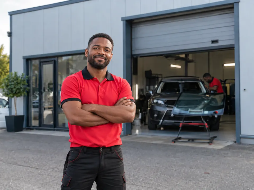 Technicien en polo rouge aux couleurs d'O'PAREBRISE 95 devant un atelier